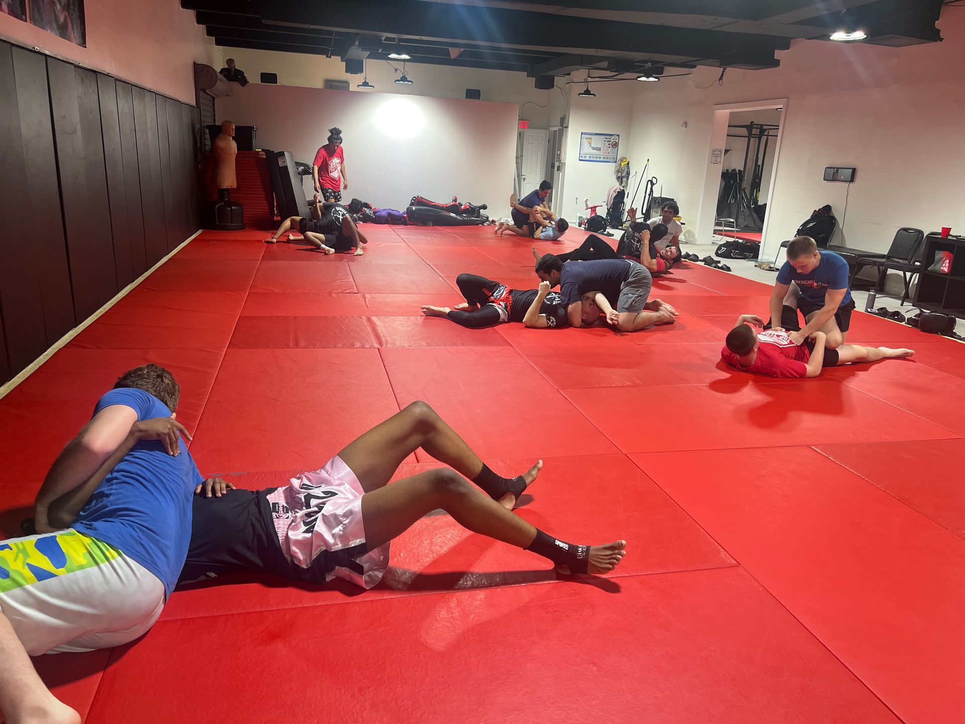 People practice grappling on red mats in a training gym.
