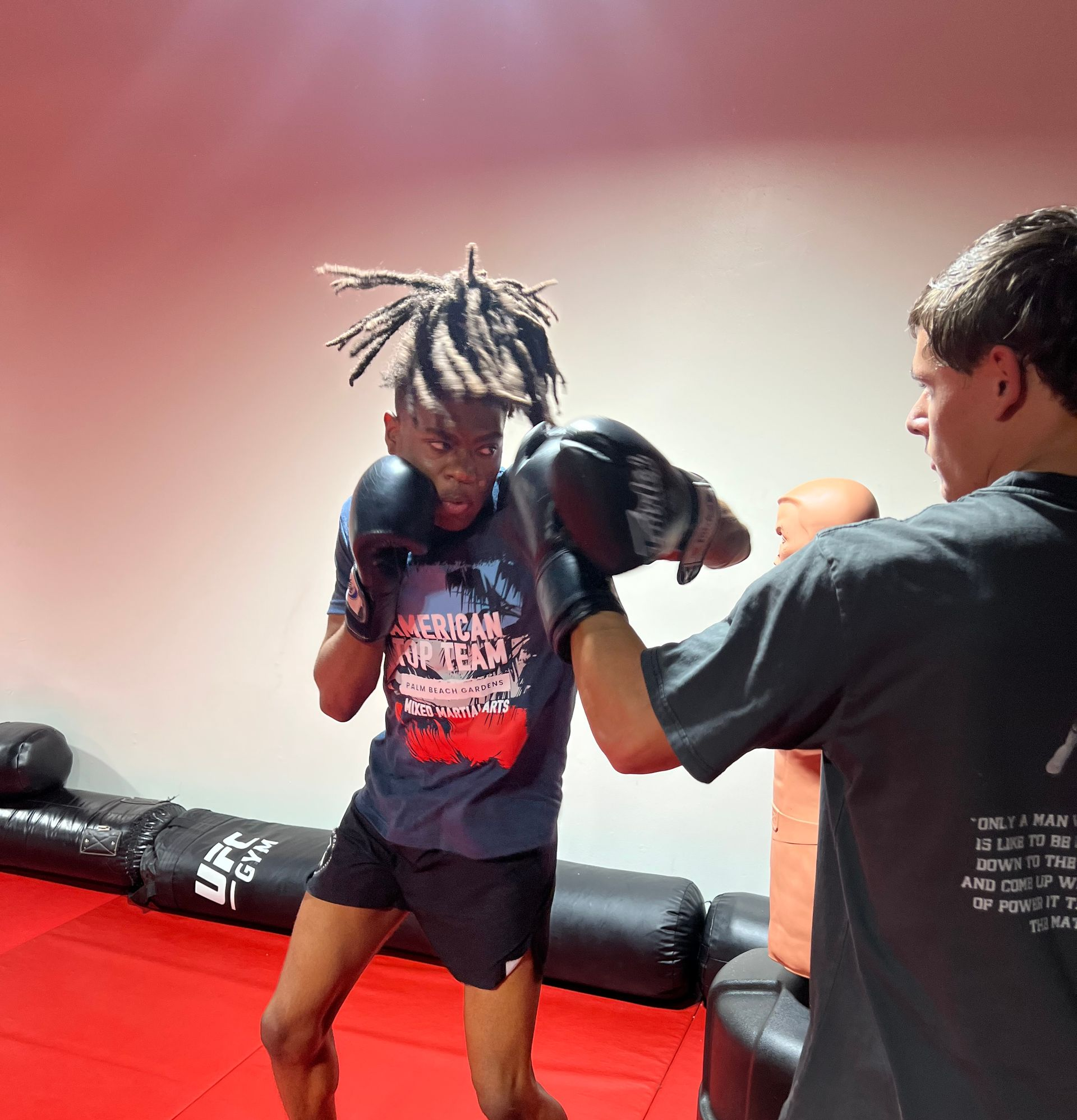 Three men are standing on a wrestling mat and one of them is wearing a yellow belt