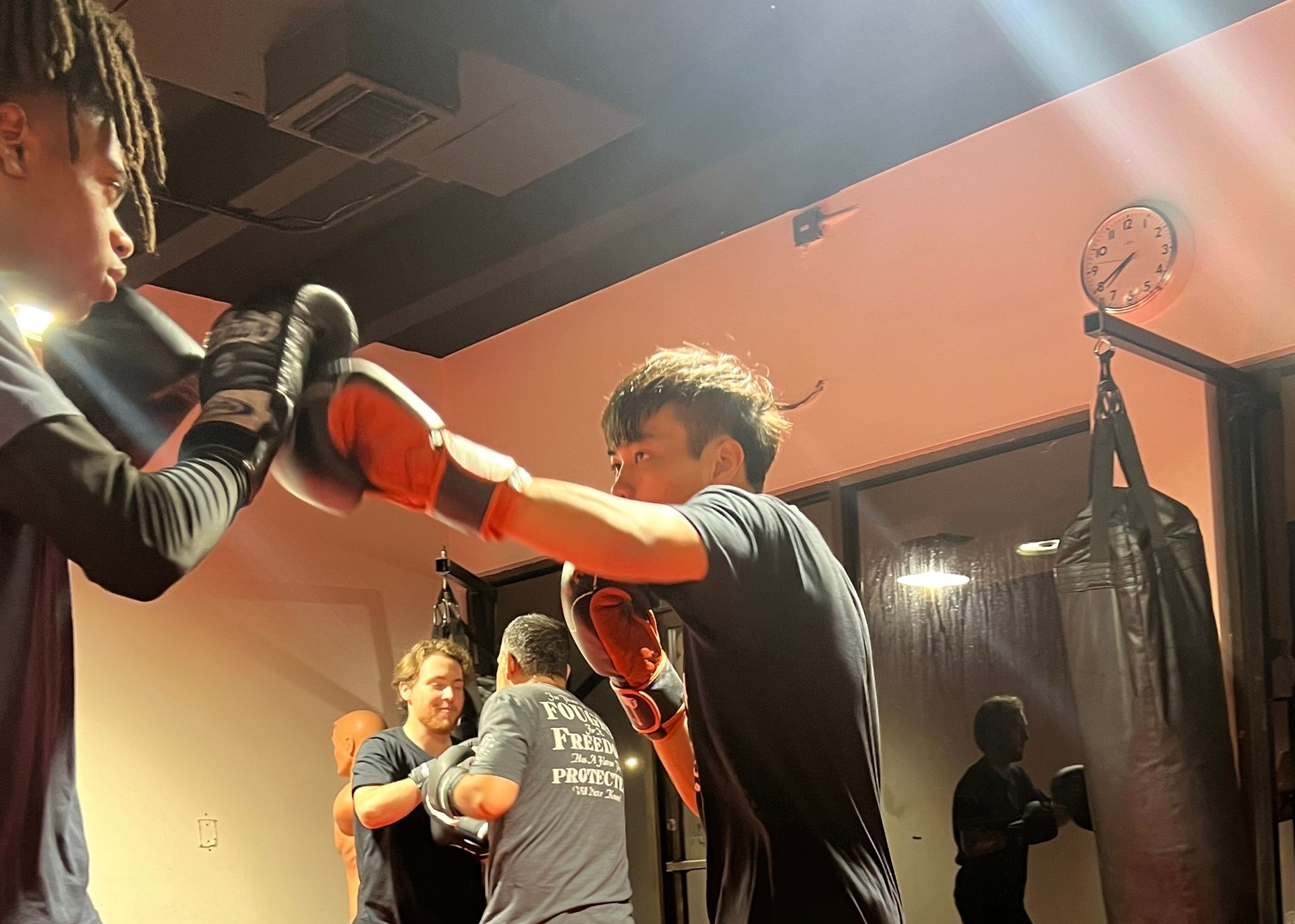 Three men are standing on a wrestling mat and one of them is wearing a yellow belt