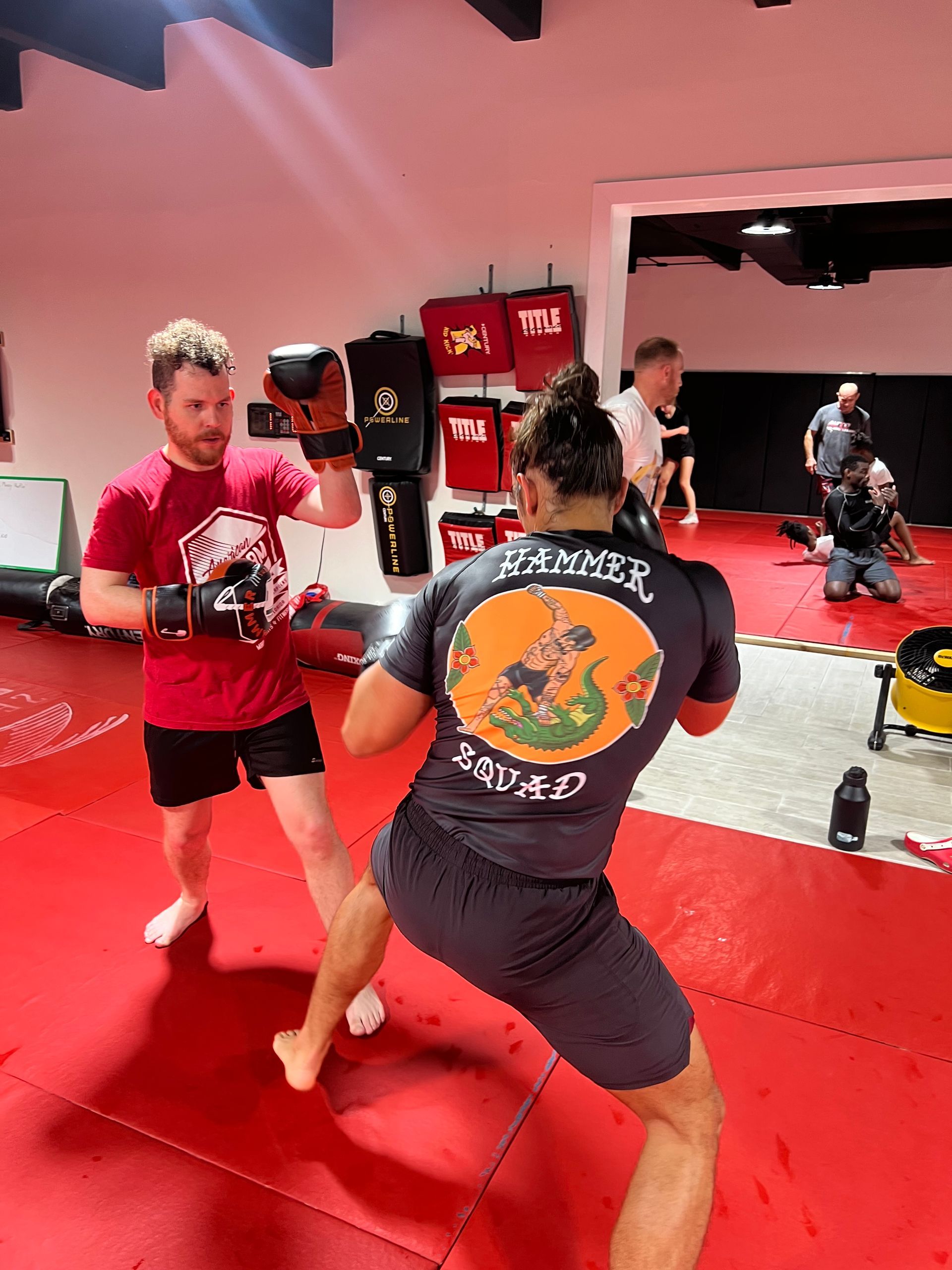 Two men are boxing on a red mat in a gym.