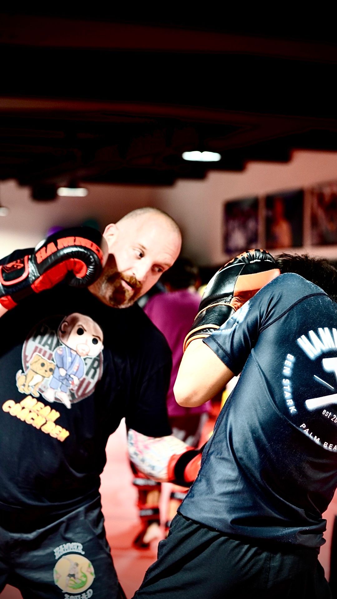 Two men are boxing in a gym and one of them is wearing a shirt with a picture of a dog on it.