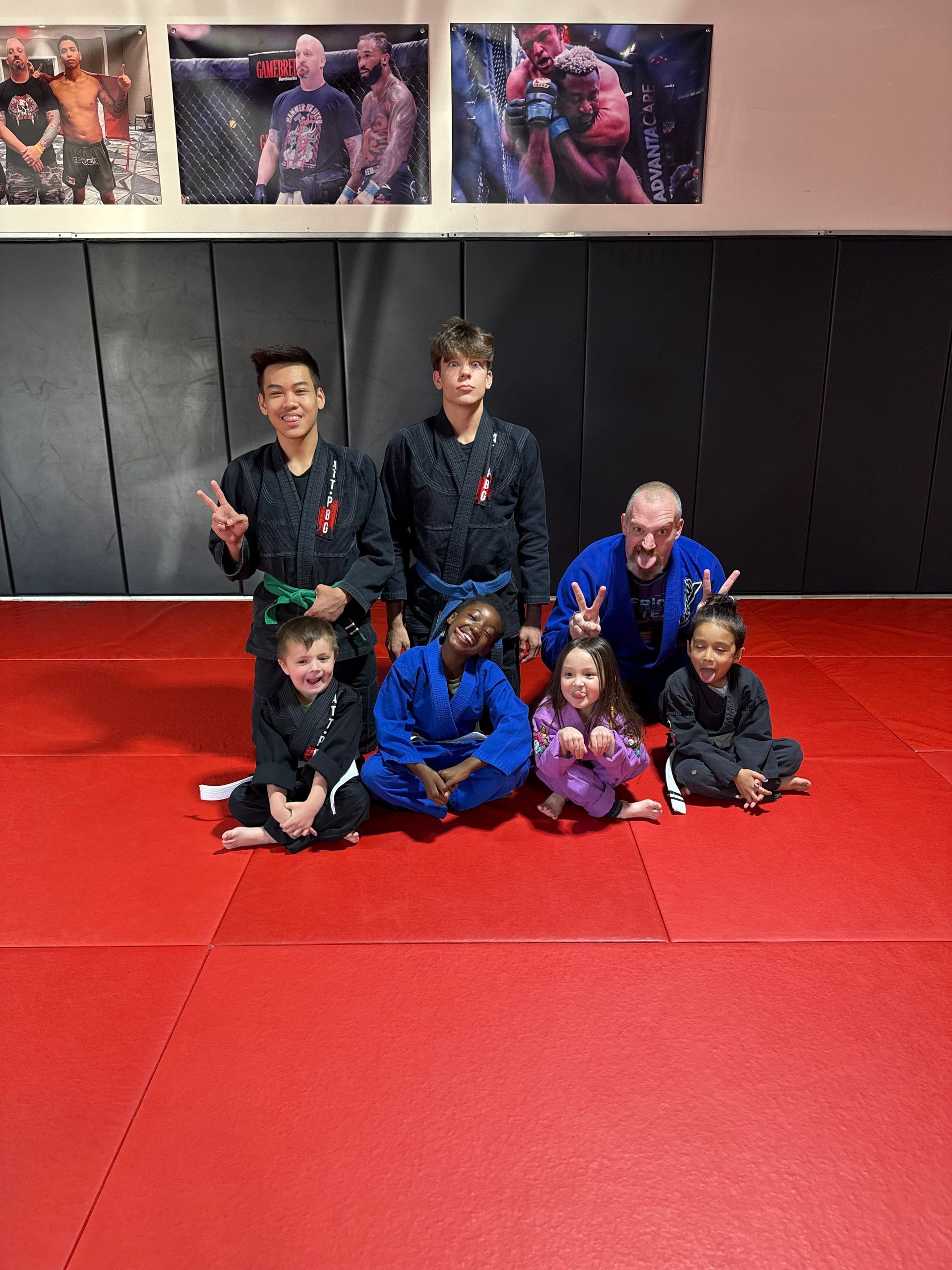 Three men are standing on a wrestling mat and one of them is wearing a yellow belt