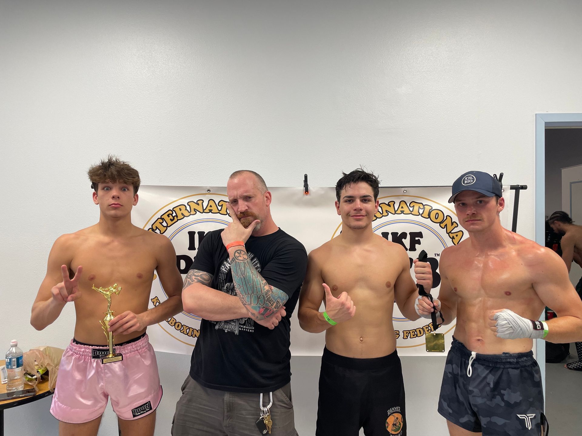 Three men are standing on a wrestling mat and one of them is wearing a yellow belt