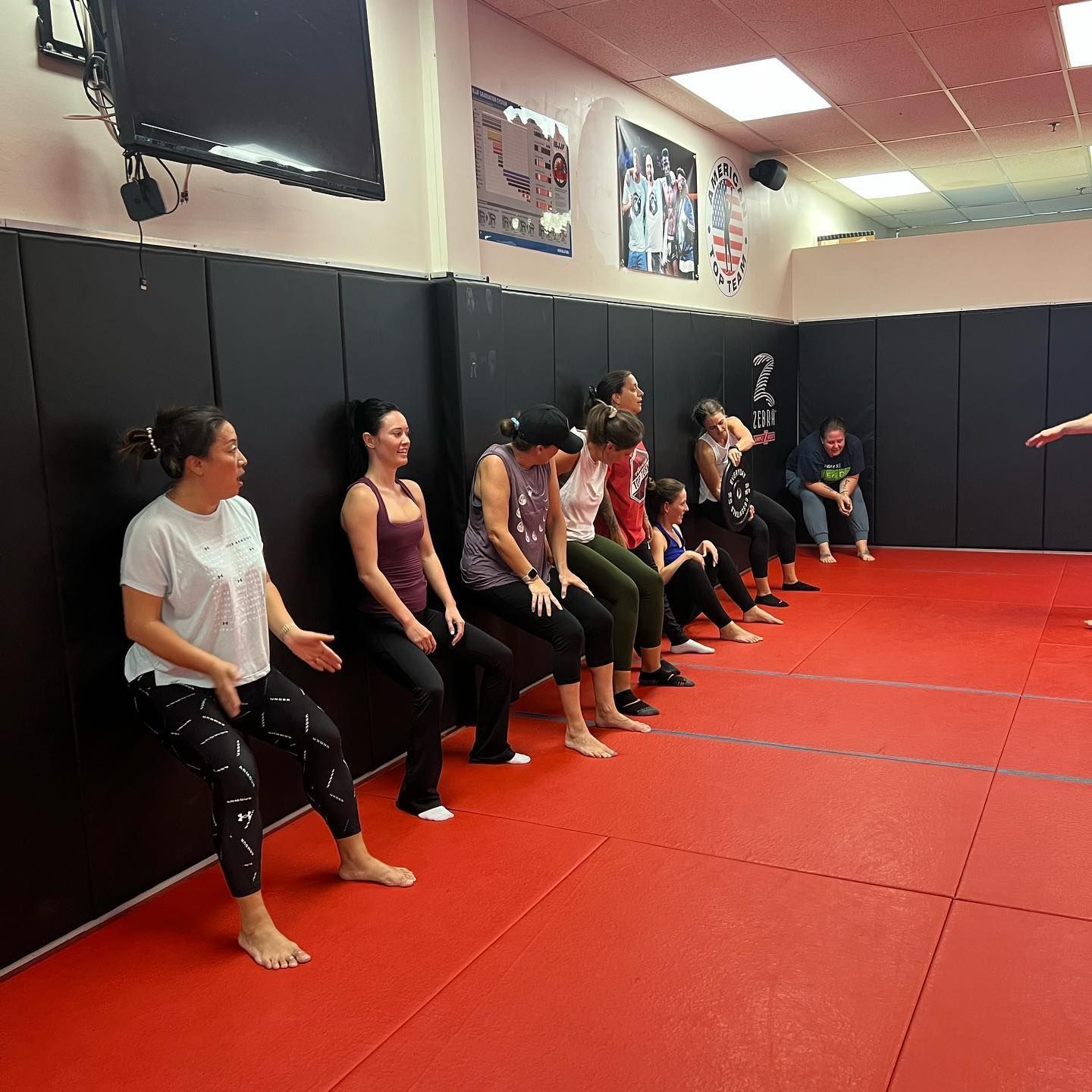 A group of people are sitting on a red mat in a gym.