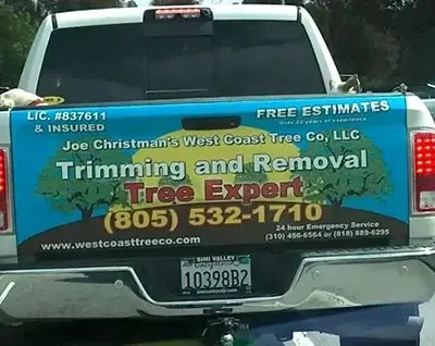 A truck with a sign on the back that says trimming and removal tree expert