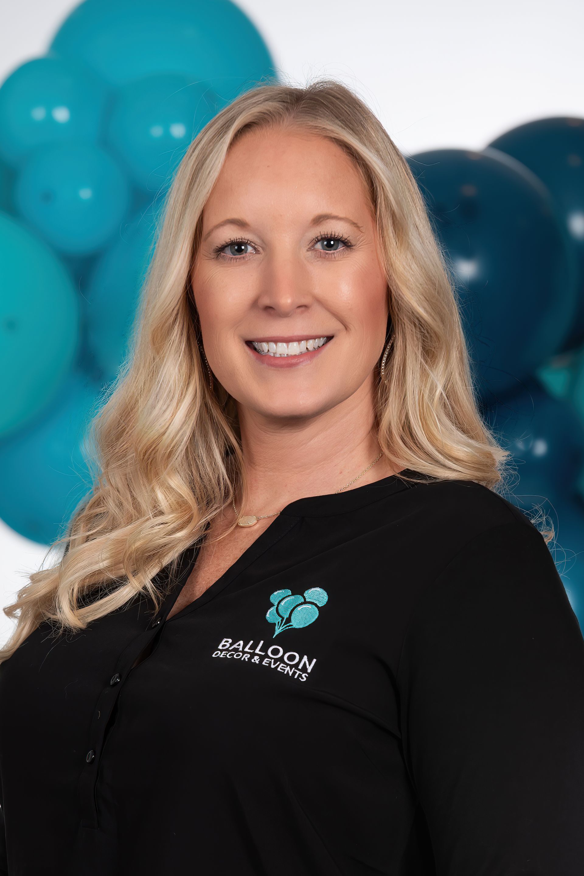 A woman is smiling in front of a bunch of blue balloons.