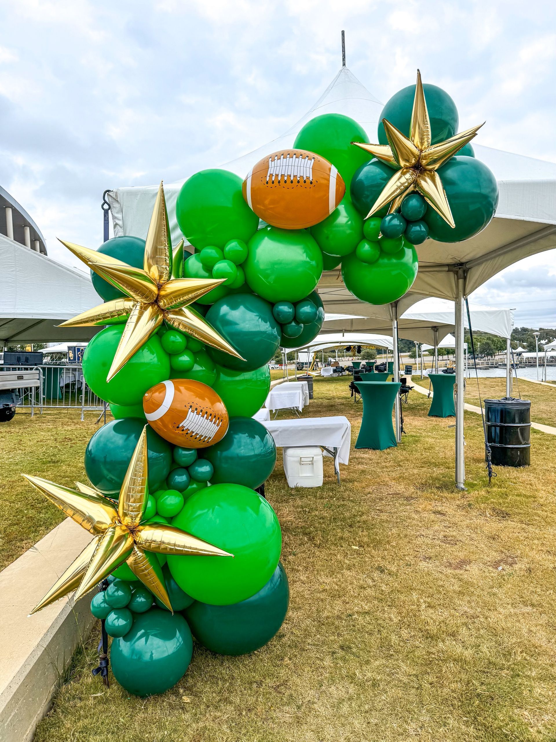 A bunch of green and gold balloons are sitting on top of a grass covered field.