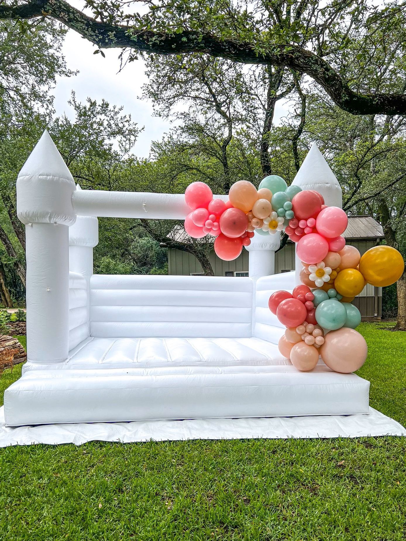 A white bouncy castle decorated with balloons is sitting on top of a lush green field.