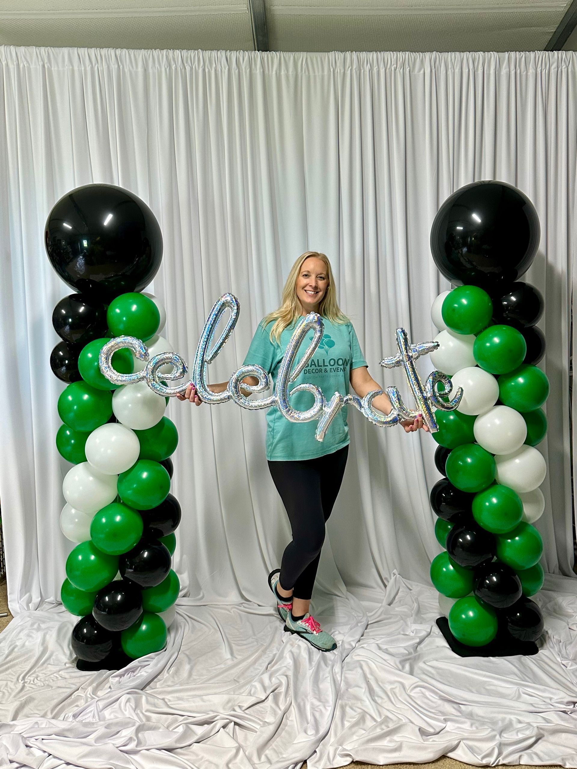 A woman is standing in front of a wall of green and black balloons.