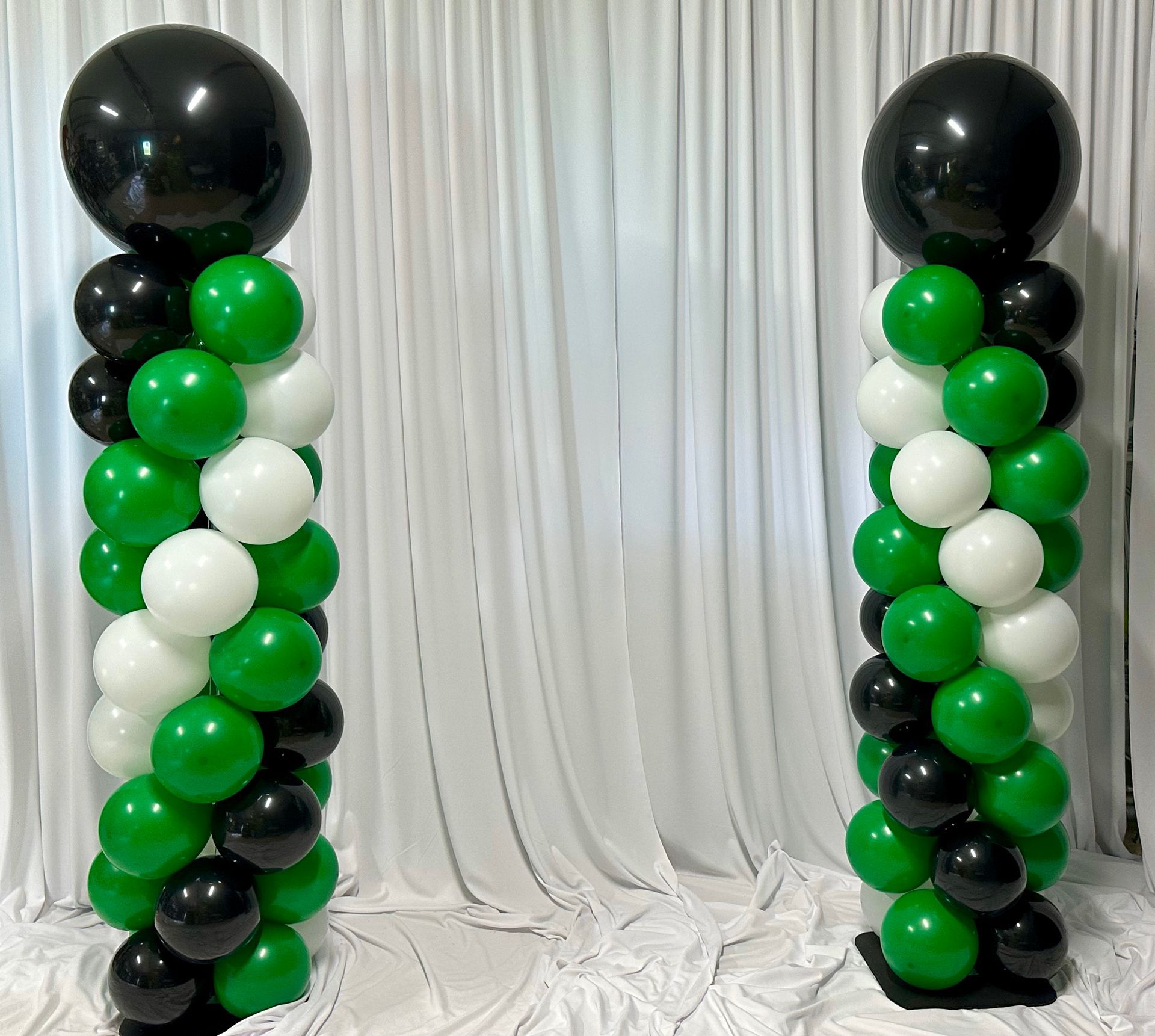 Two columns made of green and black balloons are sitting on a table.
