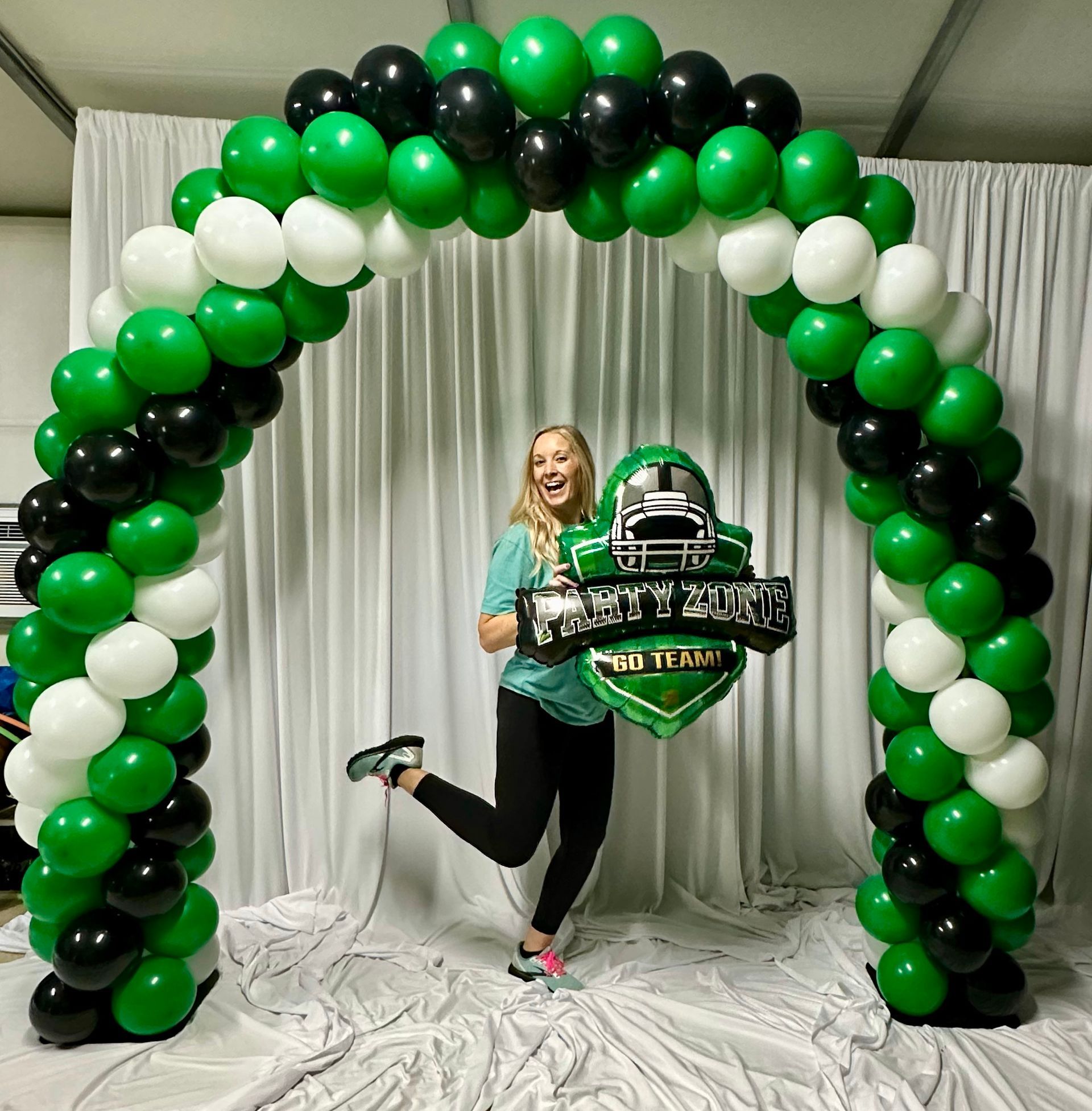 A woman is standing in front of a green and black balloon arch.