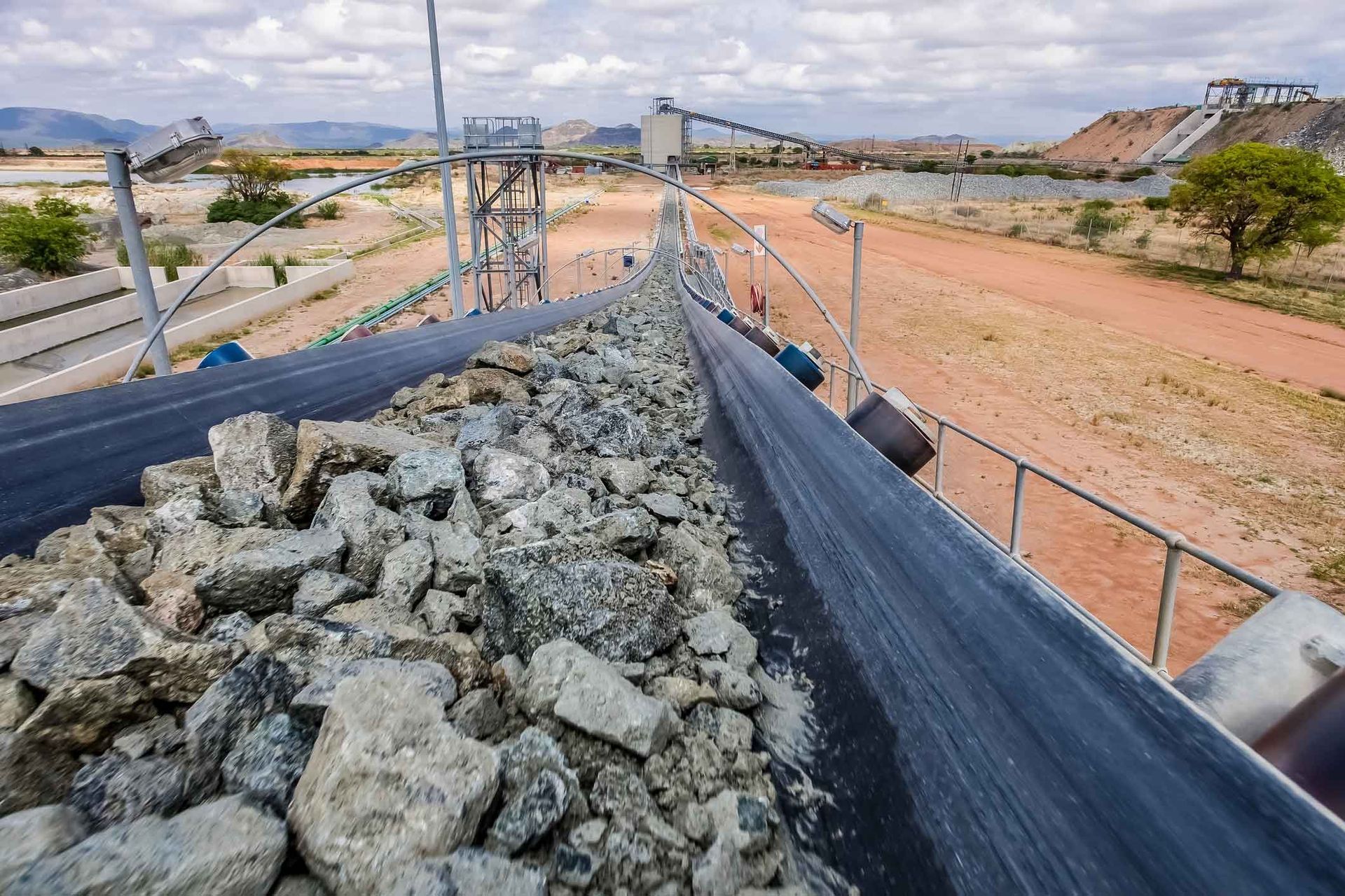 A conveyor belt filled with rocks is going down a dirt road.