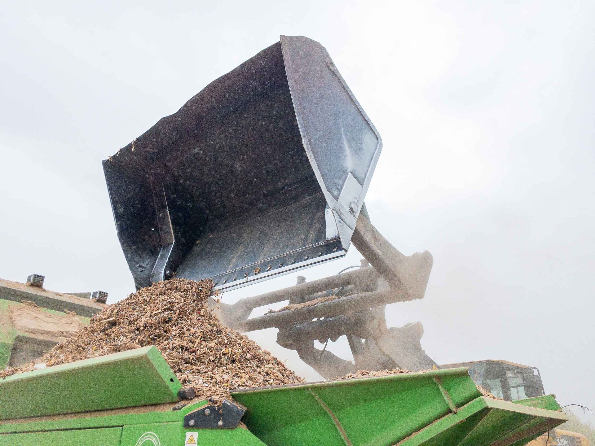 A large bucket is being poured into a pile of wood chips