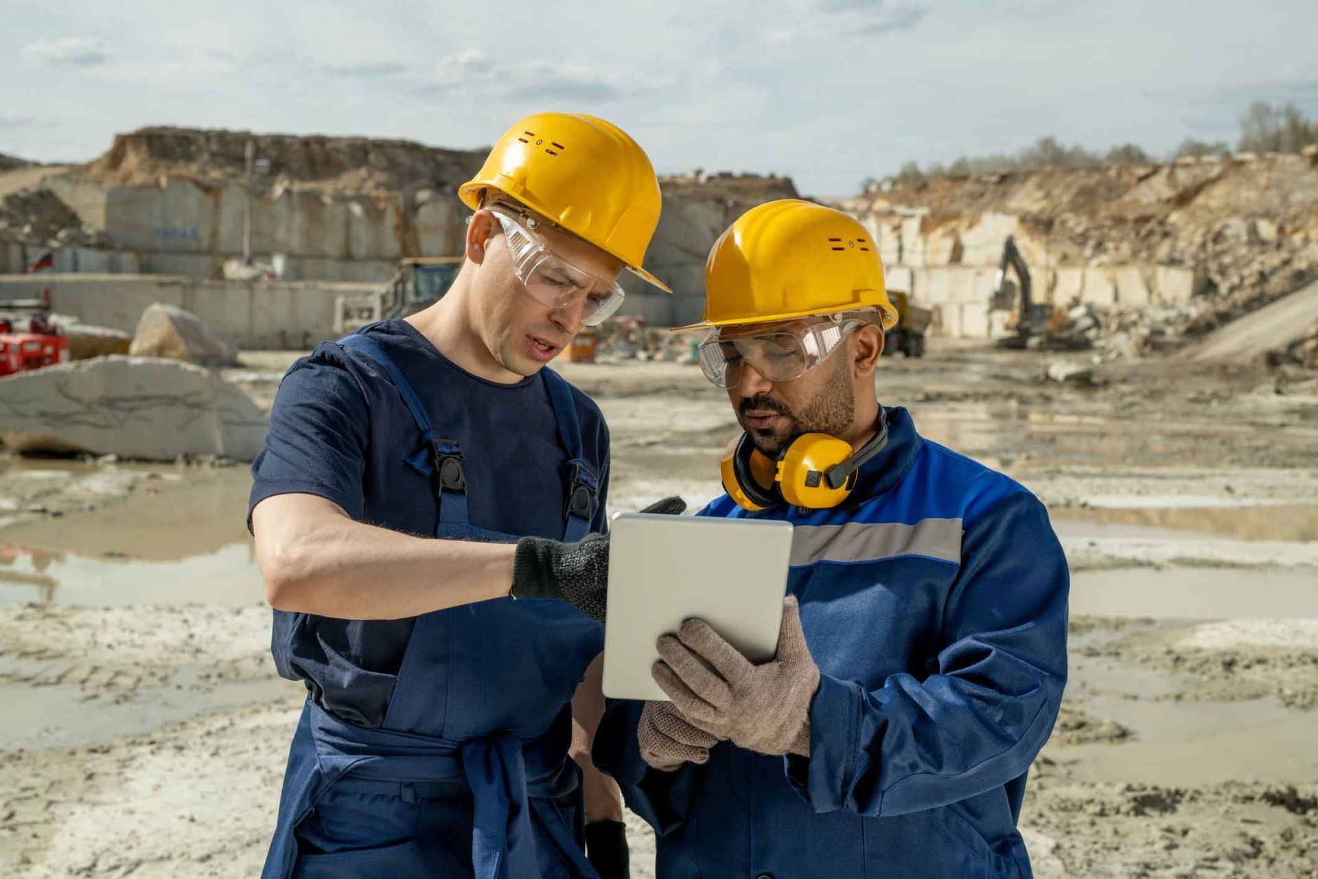Two construction workers are looking at a tablet in a quarry.