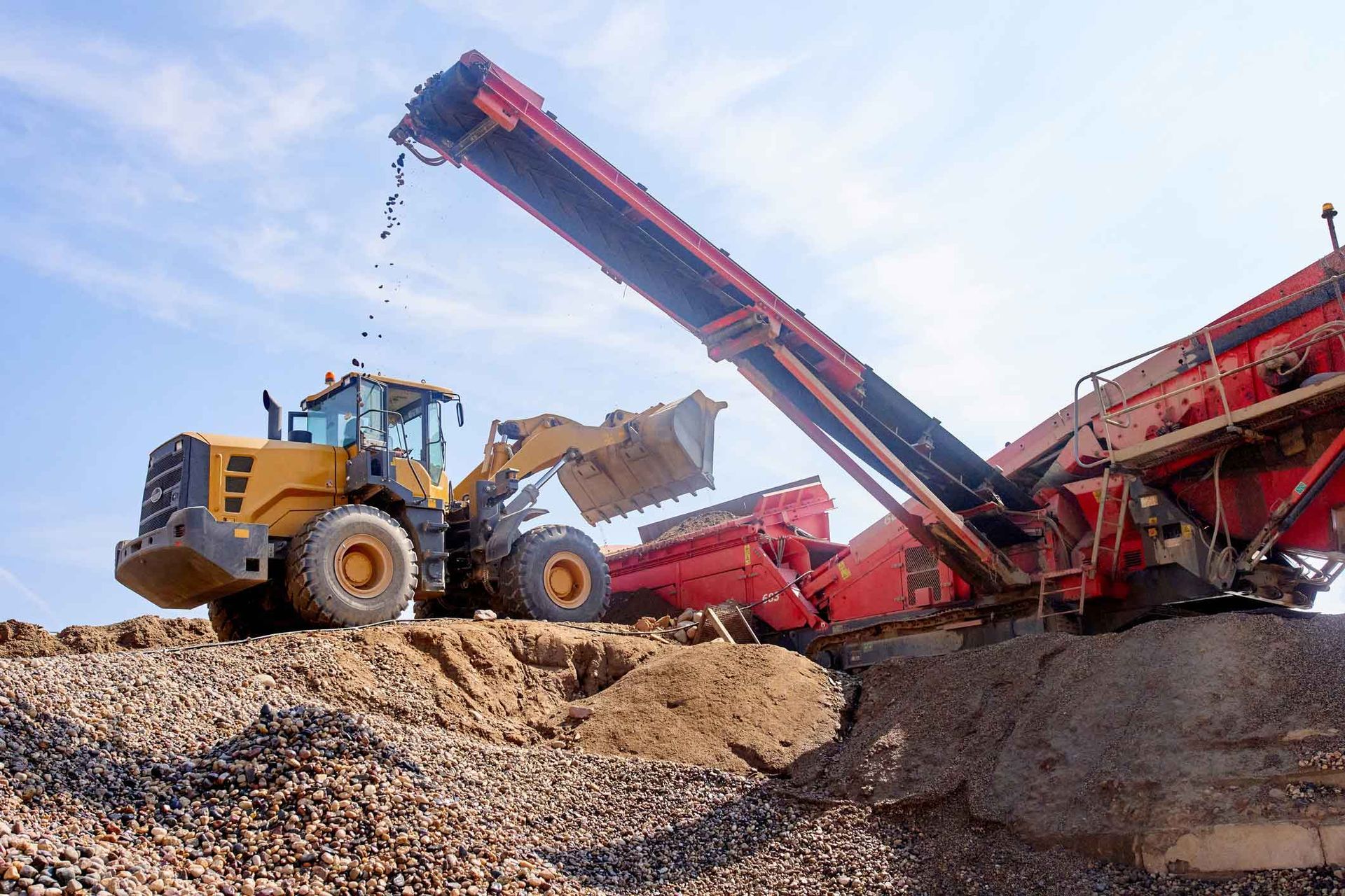 A bulldozer is loading gravel into a conveyor belt.