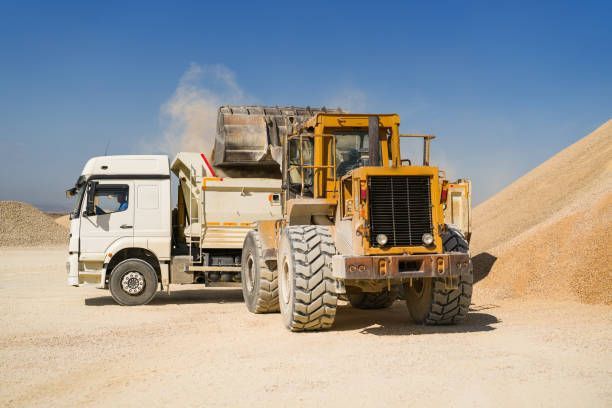 A dump truck and a bulldozer are parked next to each other in a dirt field.