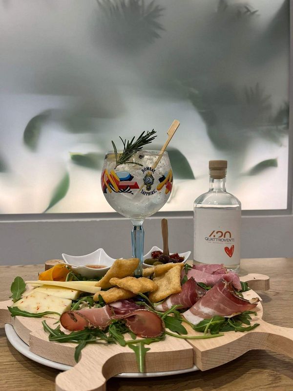 Un tagliere di legno con del cibo e un bicchiere di gin sopra.