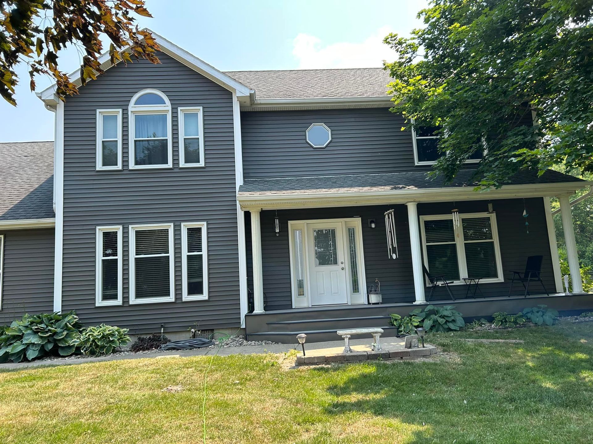 A large house with a porch and a lot of windows is sitting on top of a lush green field.