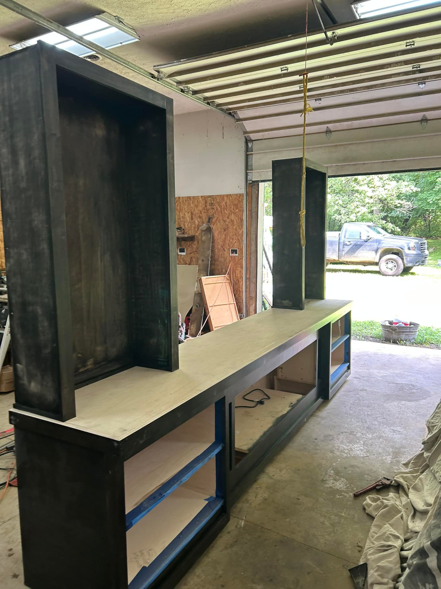 A wooden shelf is being built in a garage with a truck parked in the background.