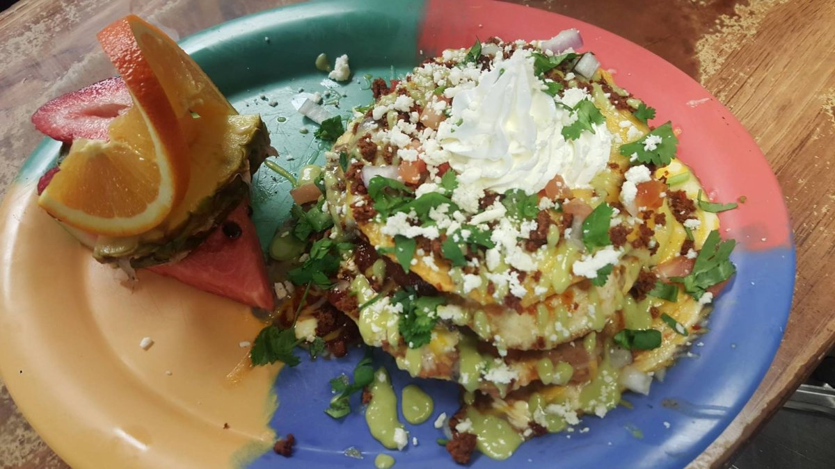 Stack of savory pancakes with toppings, garnished with fruit on a colorful plate.