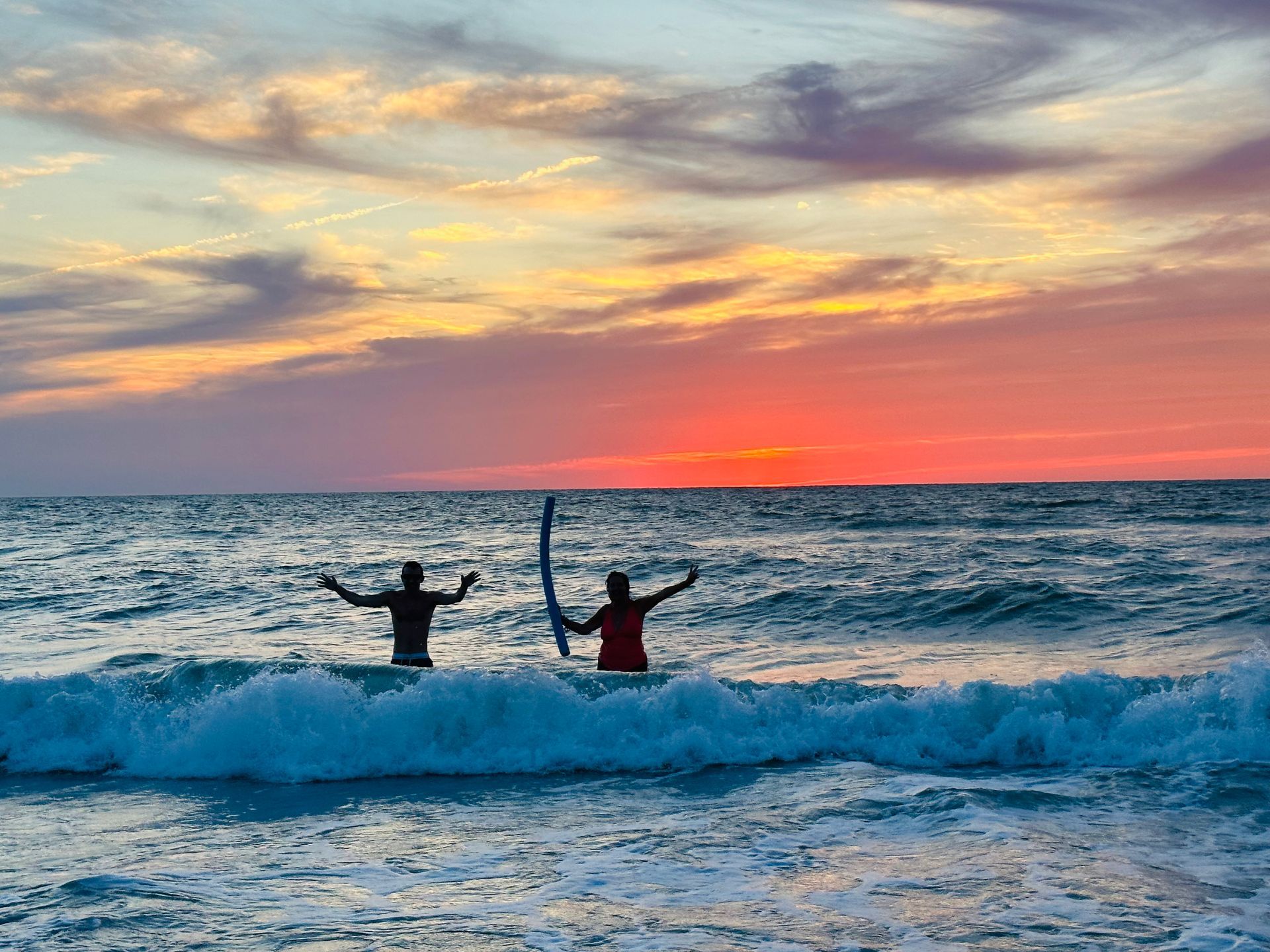 Two people are surfing in the ocean at sunset.