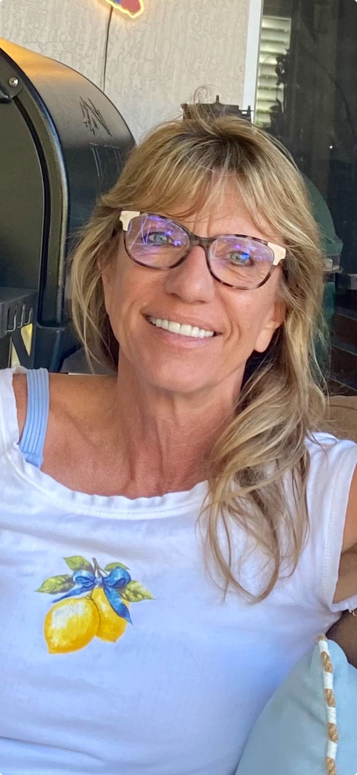 Woman wearing glasses smiling, in a white shirt with lemon print.