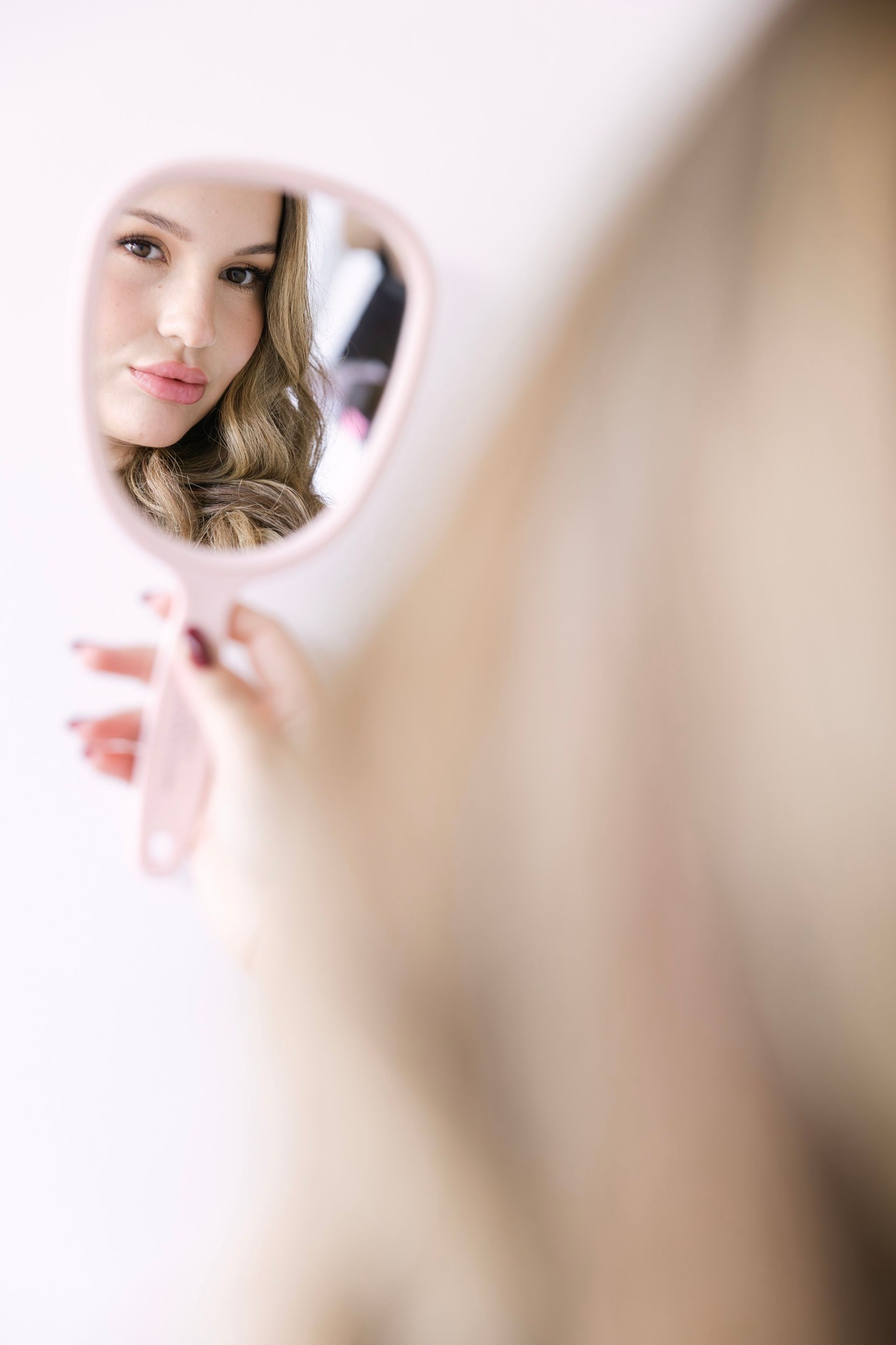 A woman holding a mirror and looking at her reflection.
