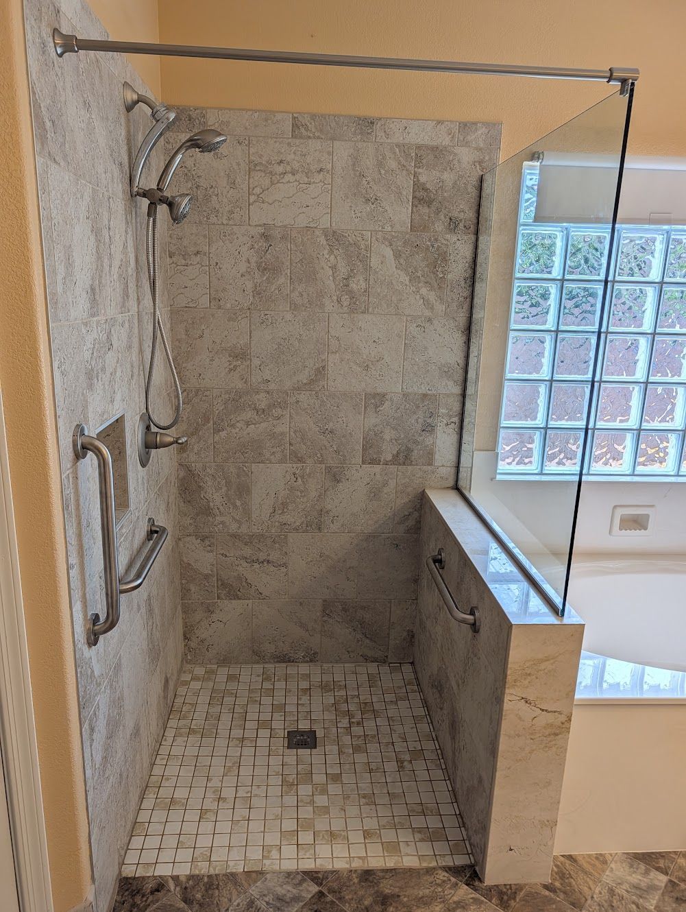 Shower with tiled walls and floor, glass enclosure, grab bars, and showerhead.