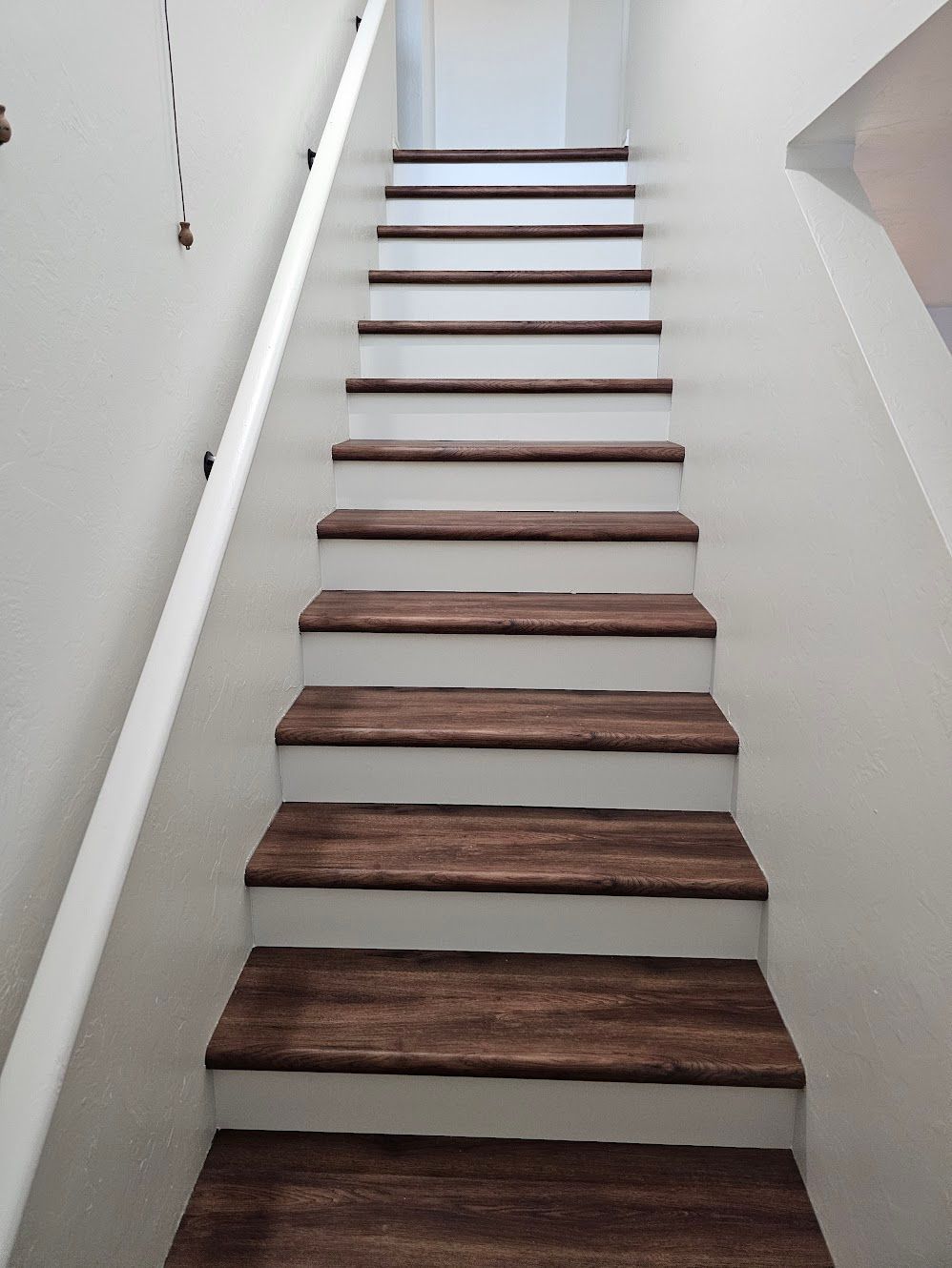 Staircase with wooden steps and white risers, ascends to an unseen space. White handrail on left.