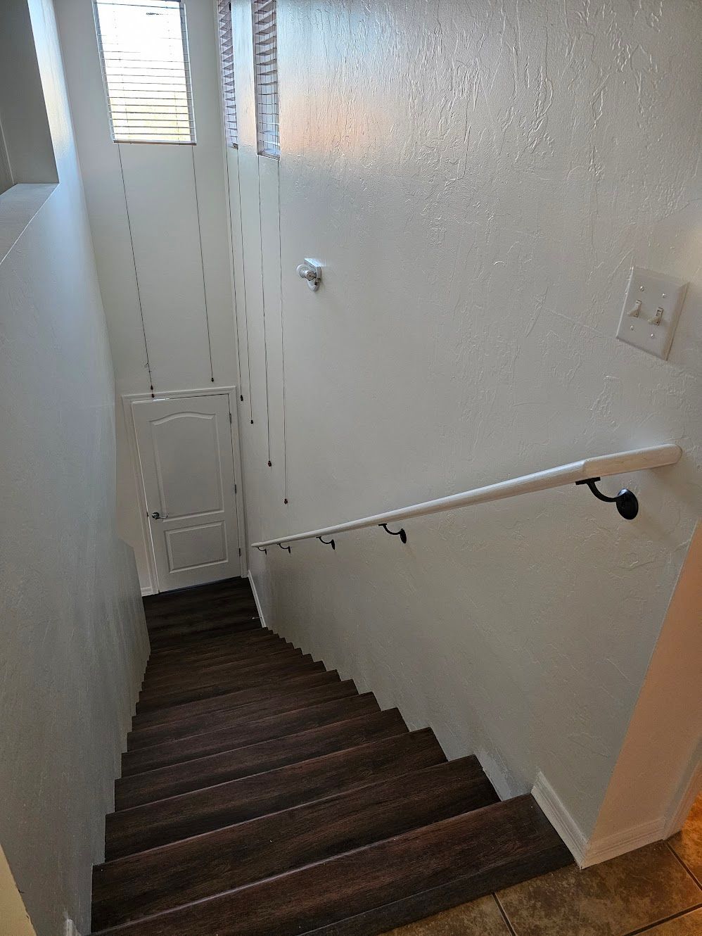 Staircase descending into a basement. Dark wooden steps, white walls, and a handrail are visible.