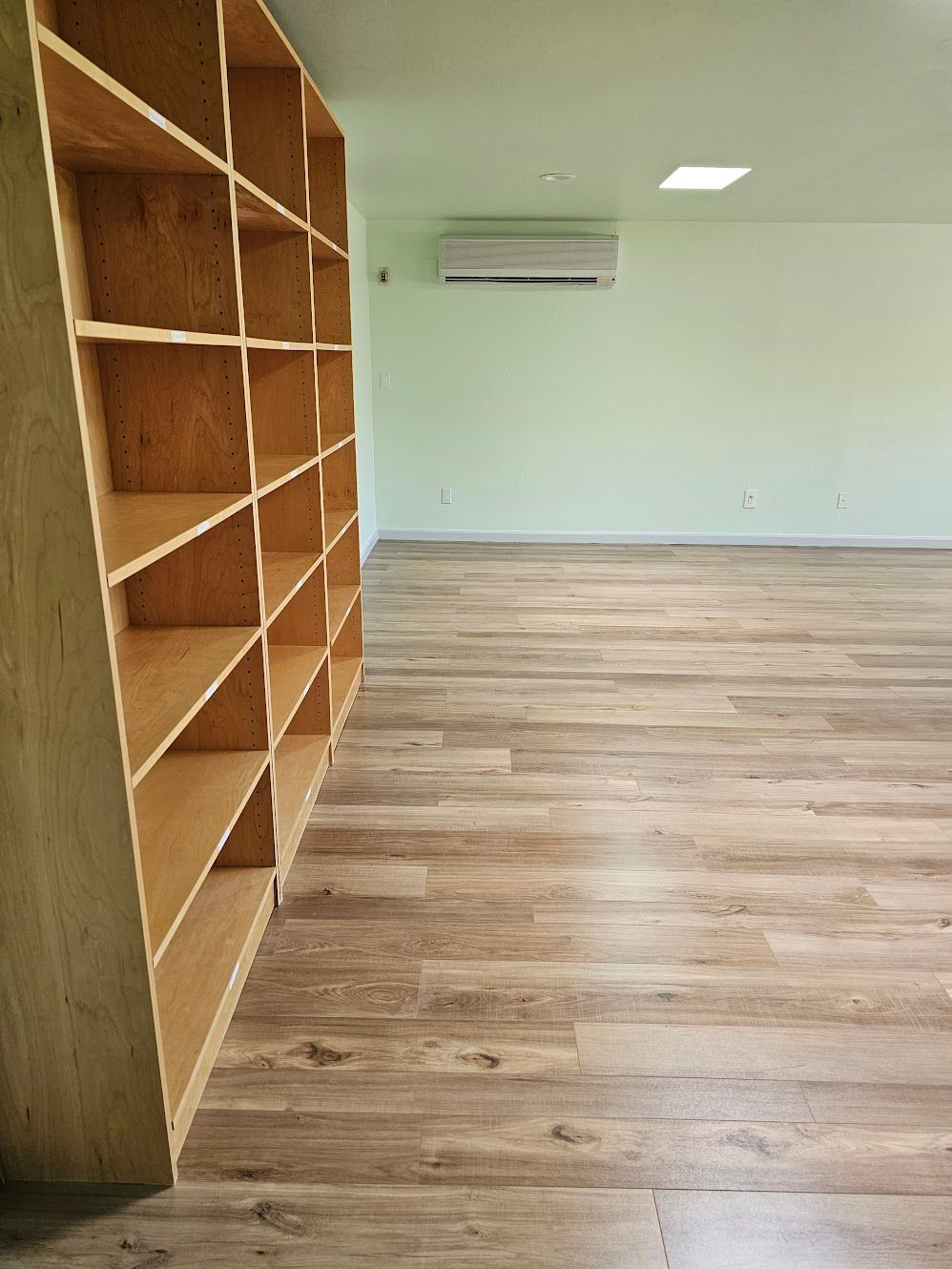 Empty room with light wood floors and large shelving unit. Air conditioner on wall.