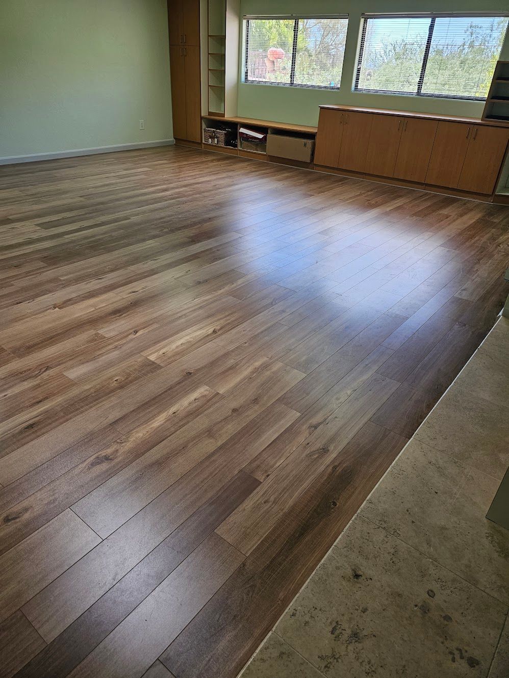 Shiny brown hardwood floor in a room with light green walls and windows.