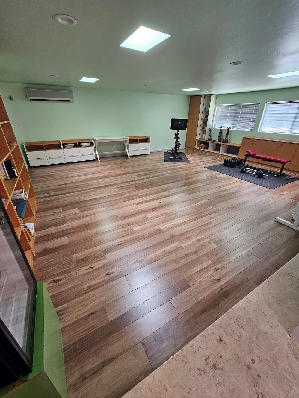 Spacious room with wood-look flooring, light green walls, a television, and gym equipment.
