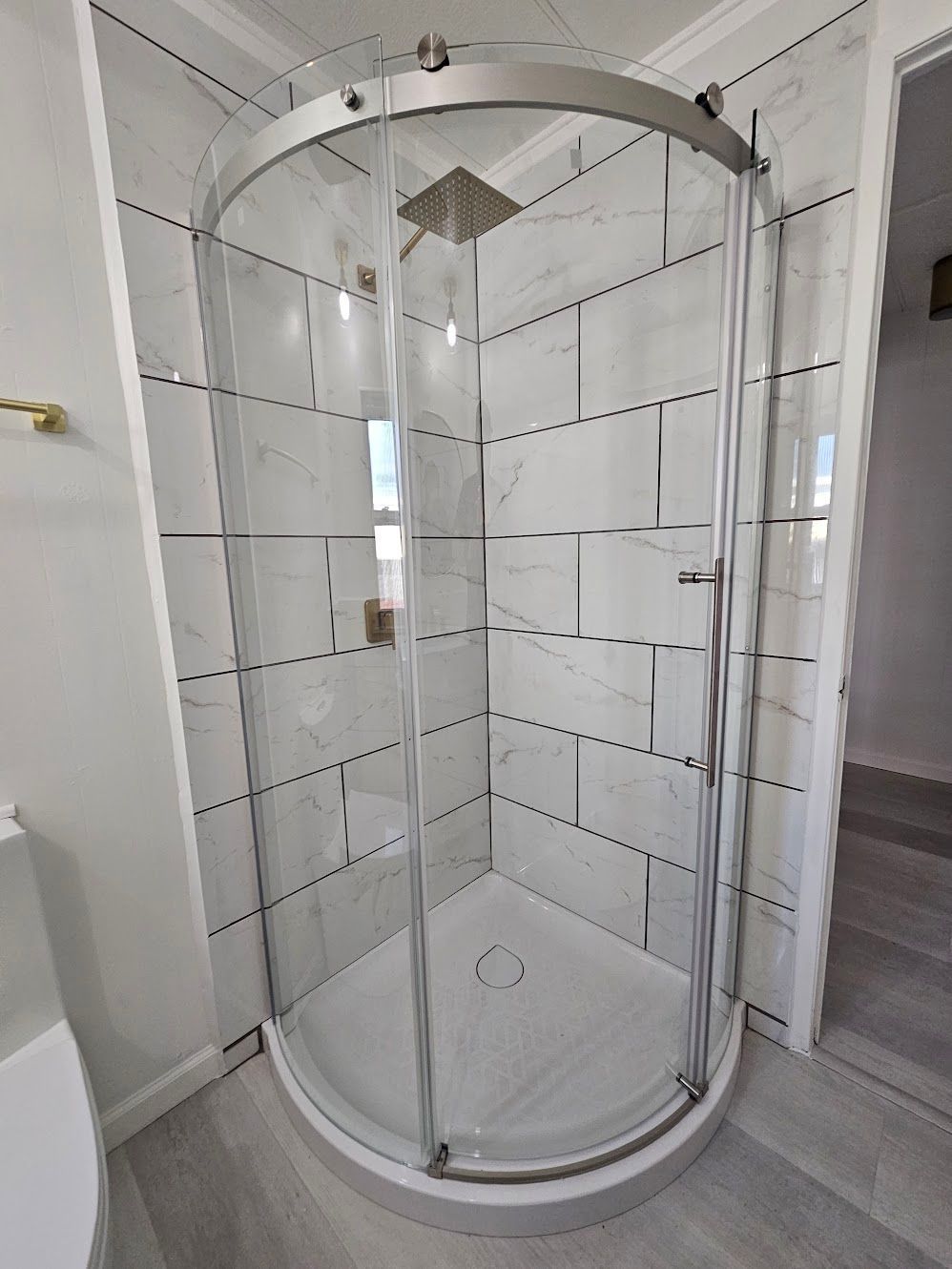 Curved glass shower enclosure with white tile walls and gray floor.