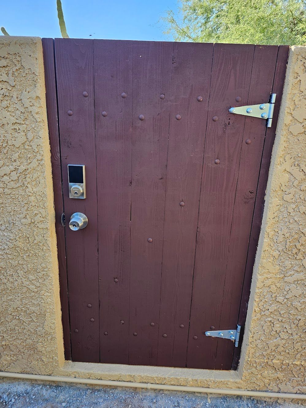 Brown wooden gate with a smart lock and hinges, set in a beige stucco wall.