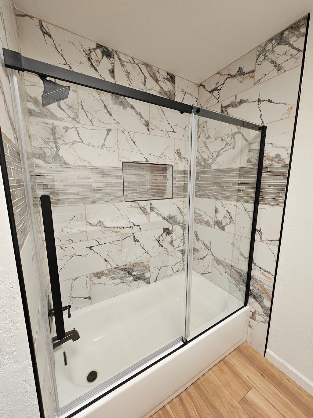 Bathroom with a white bathtub, marble tile walls, and a black-framed sliding glass shower door.