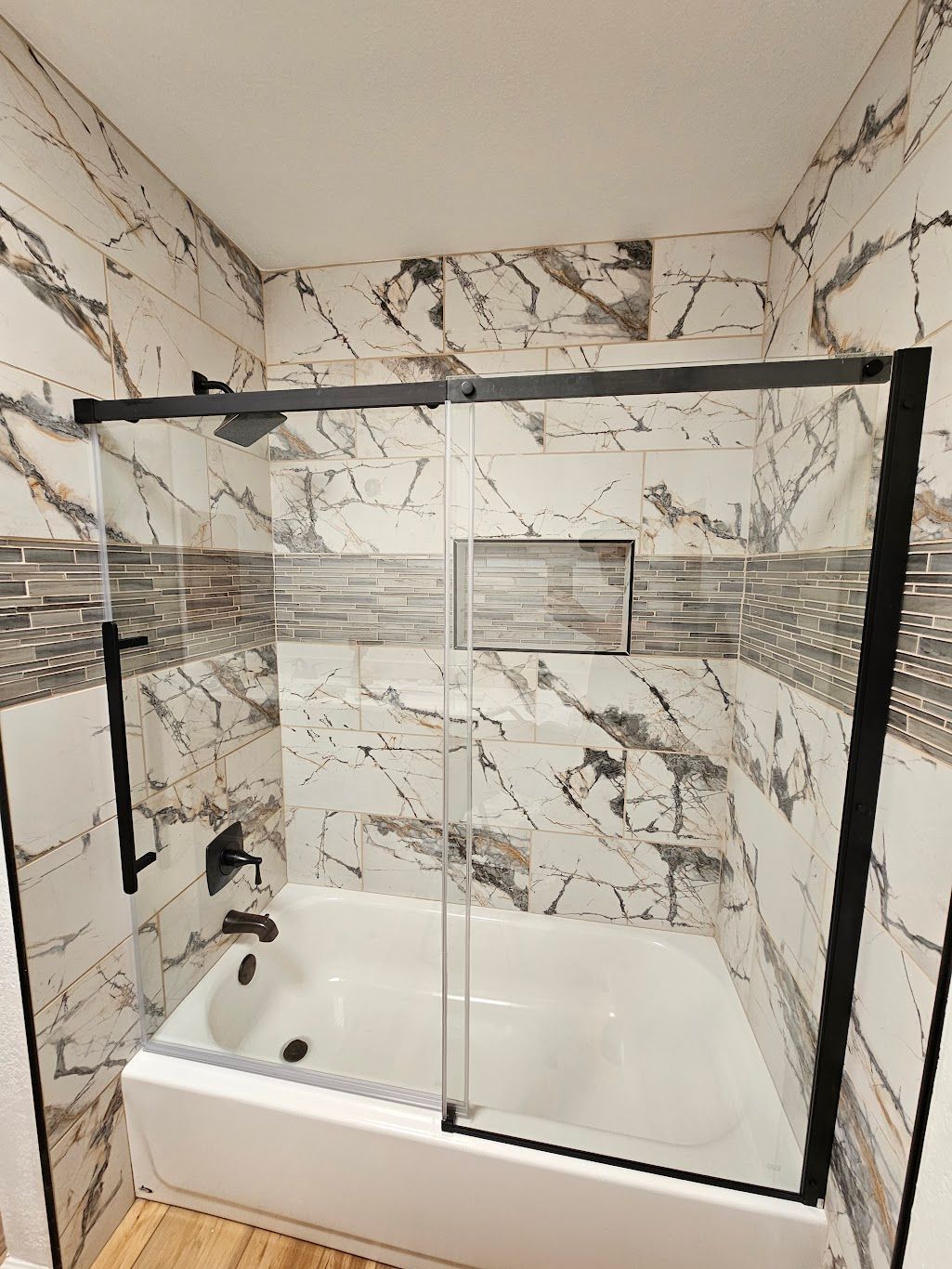 Bathroom with a white bathtub, black shower frame, and marble-patterned tile walls.