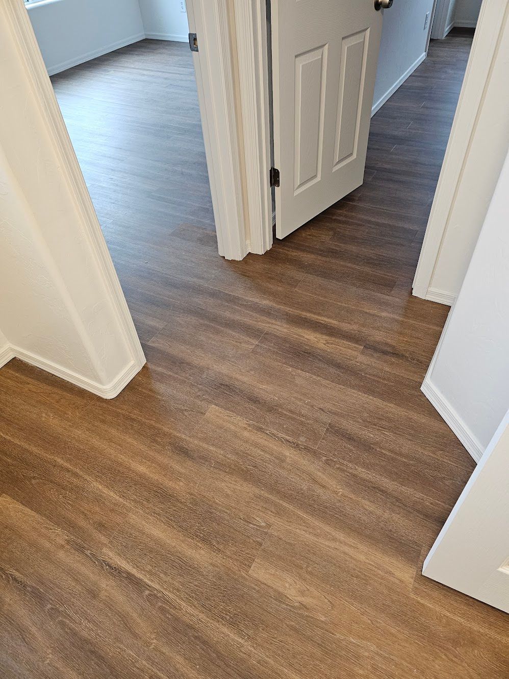 Brown plank flooring in a hallway with a partially open white door and white trim.