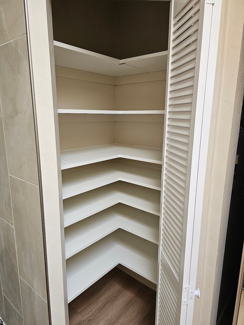 A white, corner pantry with adjustable shelves, open louvered doors.