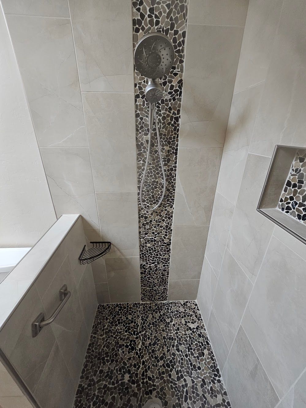 Shower with gray and beige tiles, mosaic accent strip, and multiple showerheads.
