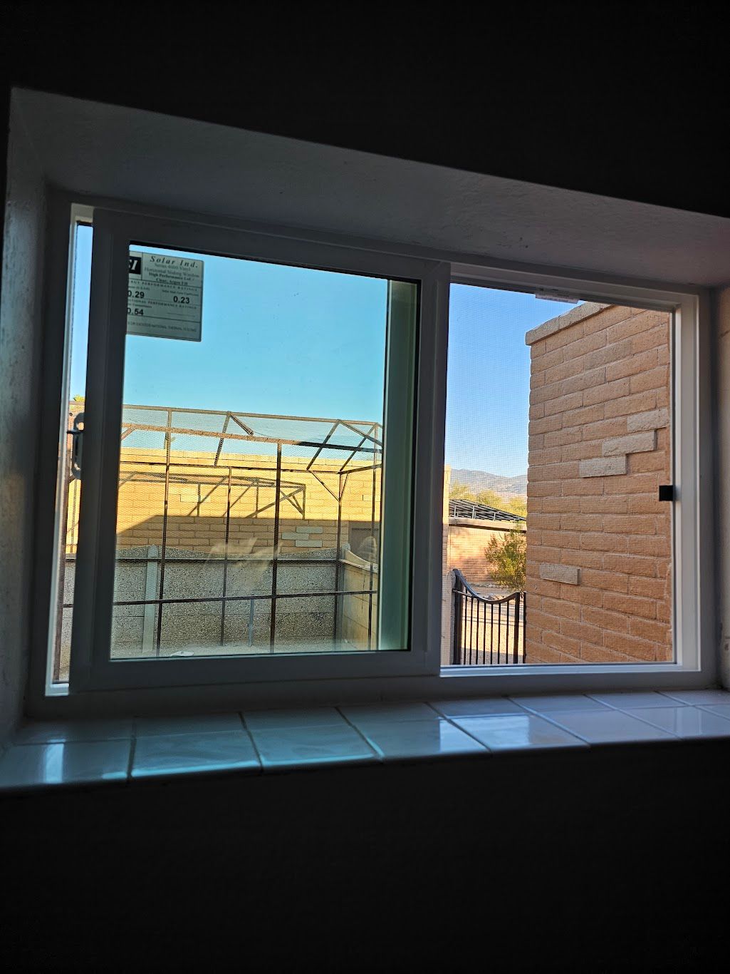 White-framed window looking out onto a brick building and a fenced area under a blue sky.