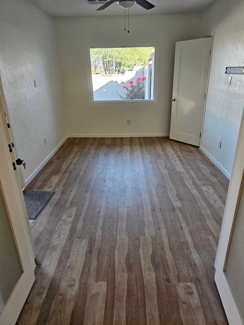 Empty room with wood-look floor, small window, white walls, closed door, and open doorway.