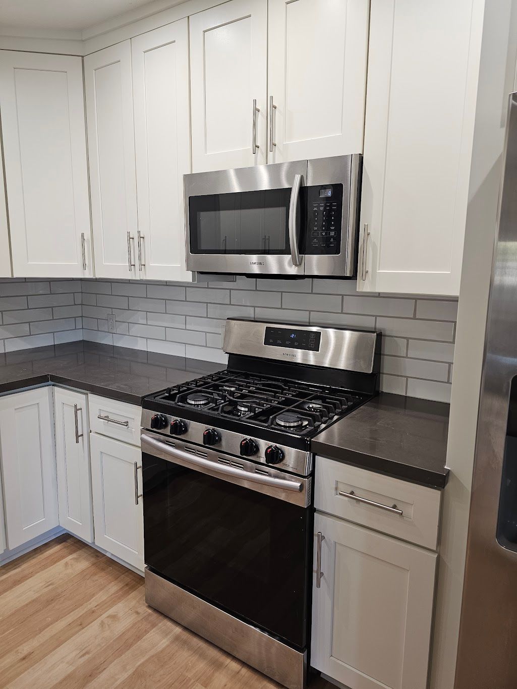 White kitchen with stainless steel appliances and dark countertops.