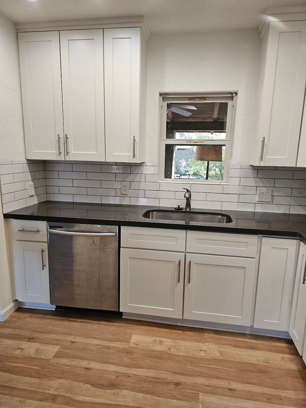 White kitchen with upper and lower cabinets, black countertop, stainless steel appliances, and a window.