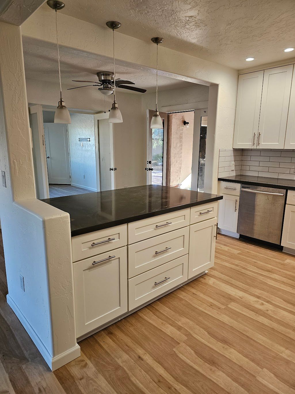 Kitchen with white cabinets, dark countertop island, stainless steel appliances, and wood flooring.