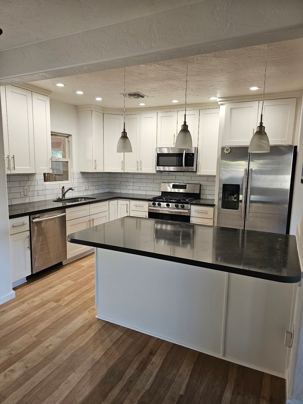 White kitchen with a black countertop island, stainless steel appliances, and wood flooring.