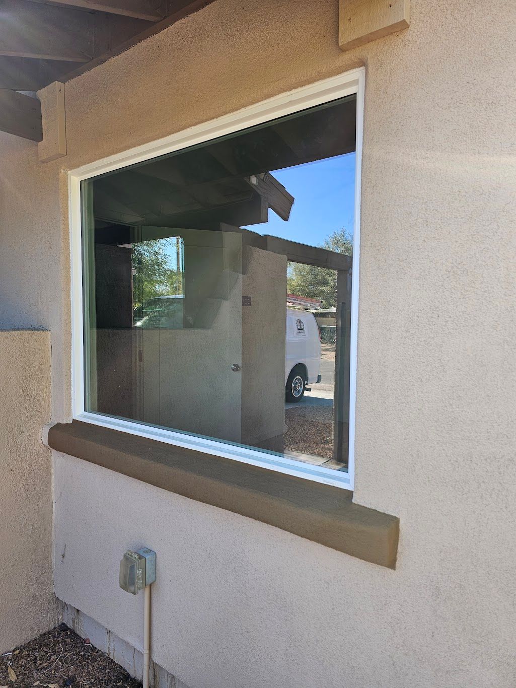 Exterior view of a window with white trim, reflecting a building and a van. The wall is light brown stucco.