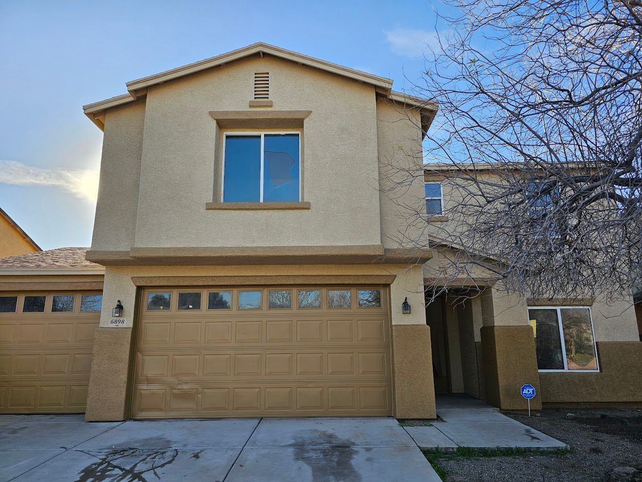 Two-story stucco house with a brown garage door and a tree to the right.