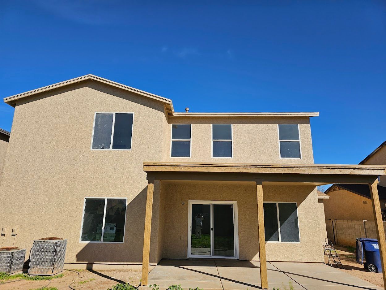 Back of a two-story beige house with large windows, covered patio, and blue sky.
