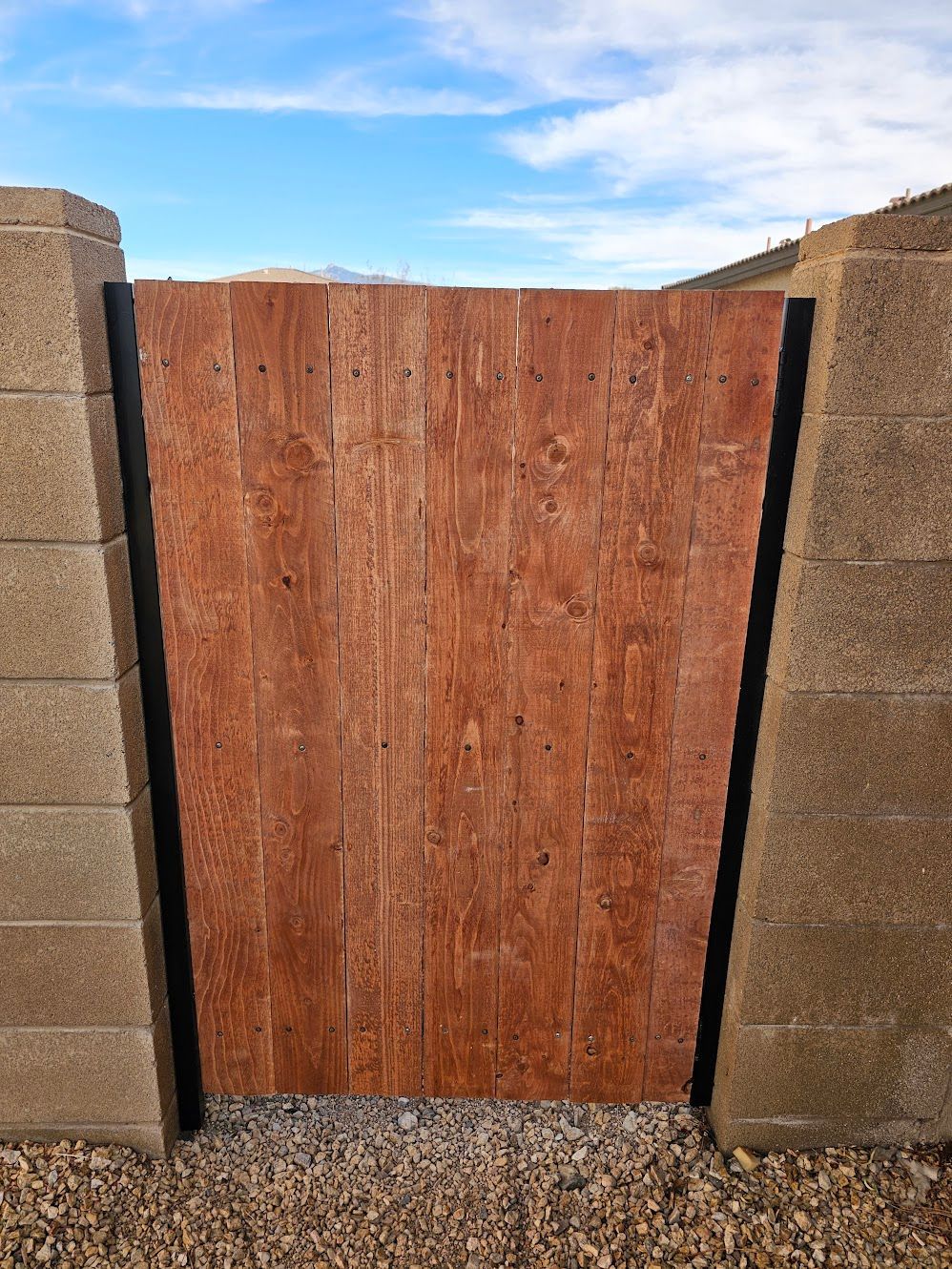 Wooden gate framed by concrete block walls against a blue sky.
